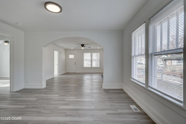 interior space featuring visible vents, a ceiling fan, arched walkways, light wood finished floors, and baseboards