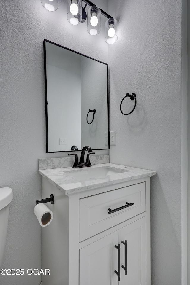 bathroom with toilet, vanity, and a textured wall