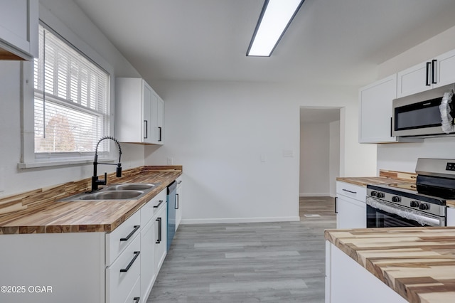 kitchen featuring butcher block counters, stainless steel appliances, light wood-style floors, white cabinetry, and a sink