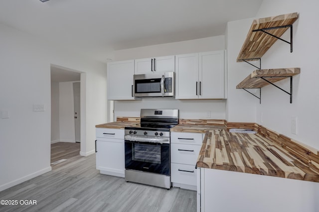 kitchen with light wood finished floors, baseboards, butcher block countertops, white cabinets, and stainless steel appliances