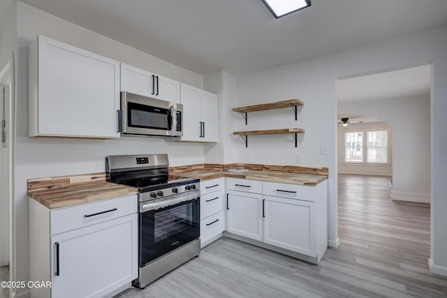 kitchen with light wood finished floors, open shelves, stainless steel appliances, wood counters, and white cabinetry