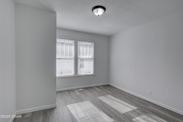 spare room with visible vents, a textured ceiling, baseboards, and wood finished floors