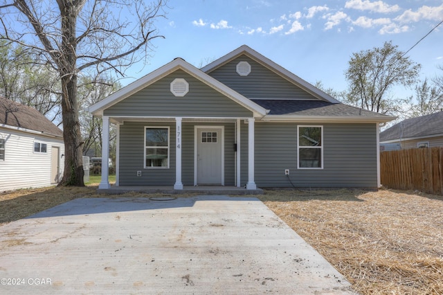 view of front facade with a porch, a shingled roof, and fence