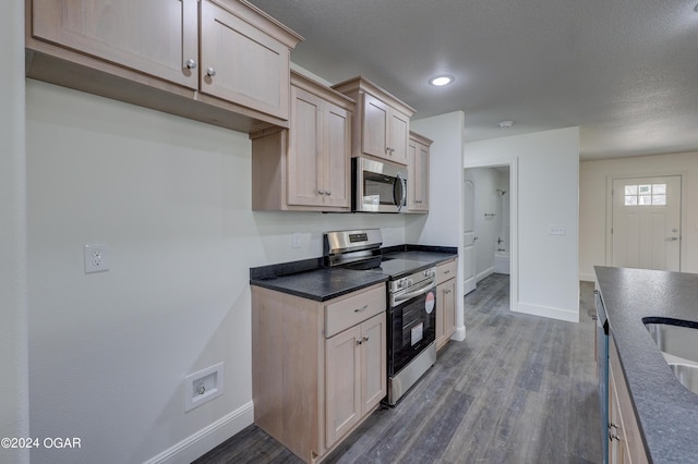 kitchen with dark countertops, baseboards, stainless steel appliances, a textured ceiling, and dark wood-style flooring