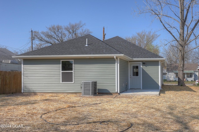 rear view of house with cooling unit, fence, and roof with shingles