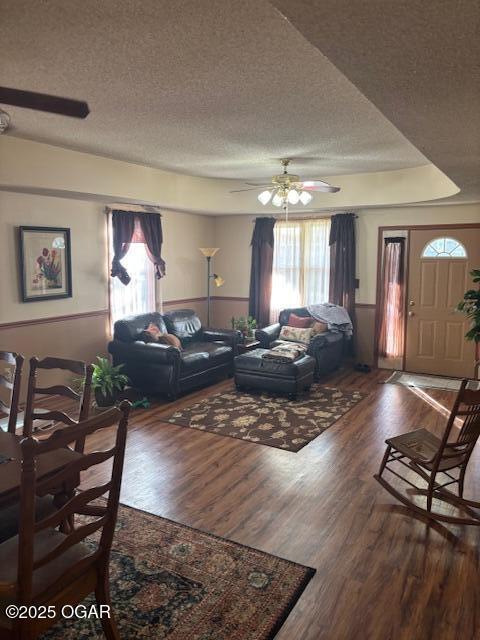 living room featuring a textured ceiling, a ceiling fan, a tray ceiling, and wood finished floors