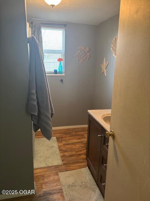 bathroom with baseboards, a textured ceiling, wood finished floors, and vanity