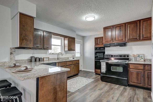 kitchen featuring light wood finished floors, a breakfast bar area, exhaust hood, black appliances, and a sink