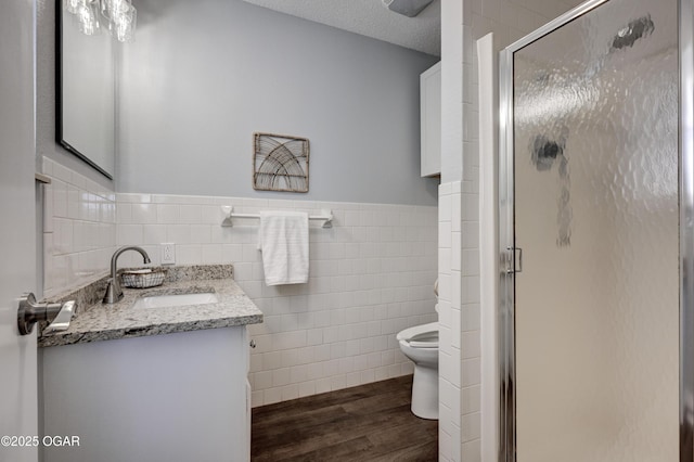 bathroom with wood finished floors, a stall shower, a textured ceiling, tile walls, and toilet