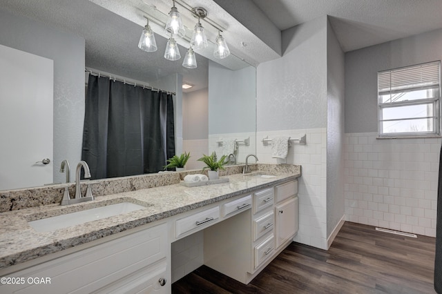 bathroom featuring wood finished floors, a textured ceiling, tile walls, and a sink