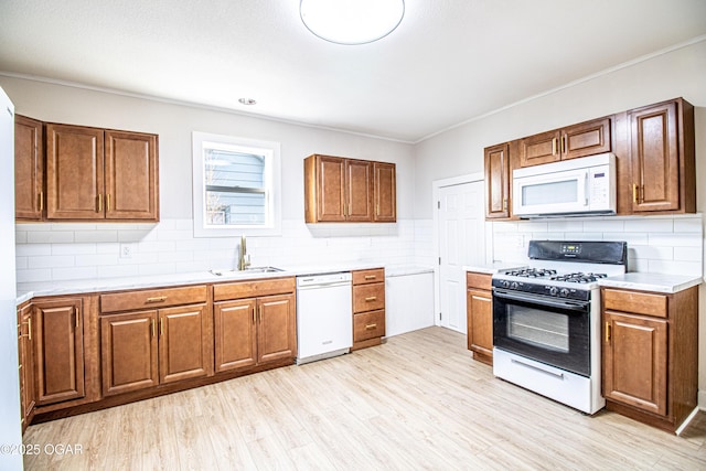 kitchen with a sink, white appliances, light wood-style floors, brown cabinetry, and light countertops