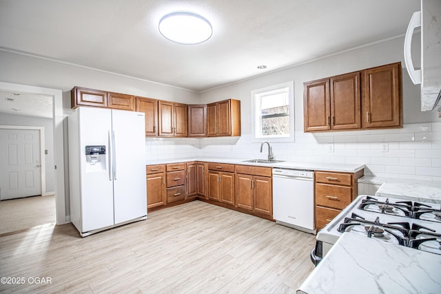 kitchen featuring backsplash, light wood-type flooring, brown cabinetry, white appliances, and a sink