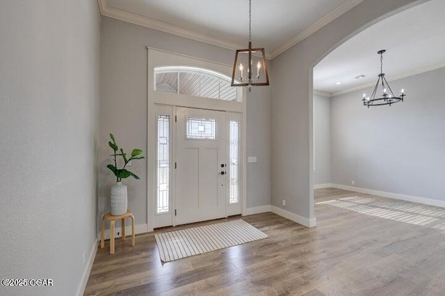 entryway featuring ornamental molding, wood finished floors, arched walkways, baseboards, and a chandelier