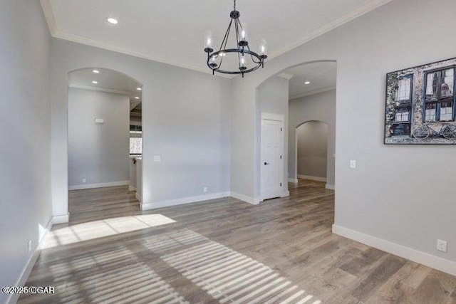 empty room featuring ornamental molding, wood finished floors, arched walkways, and baseboards