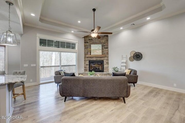 living room featuring baseboards, a fireplace, ornamental molding, a raised ceiling, and light wood-type flooring