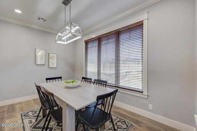 dining room featuring visible vents, wood finished floors, baseboards, and ornamental molding