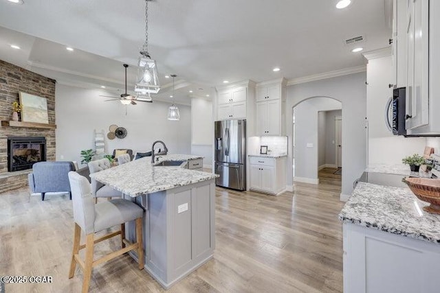 kitchen with appliances with stainless steel finishes, a fireplace, arched walkways, a ceiling fan, and a sink