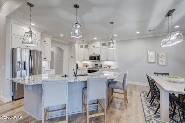 kitchen featuring stainless steel appliances, arched walkways, a kitchen breakfast bar, and white cabinetry