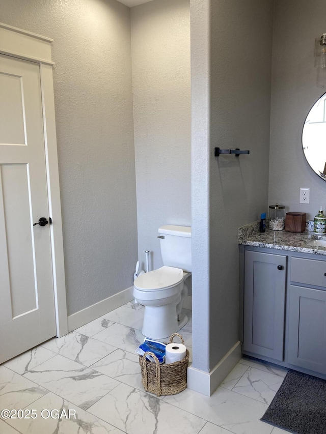 bathroom featuring vanity, toilet, baseboards, and marble finish floor