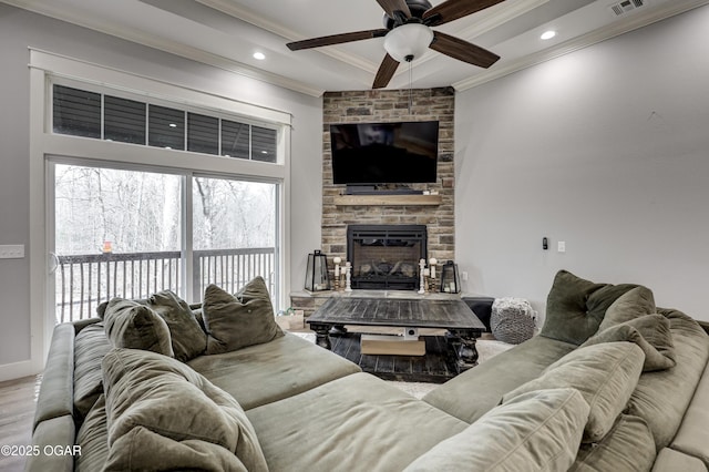 living room featuring visible vents, crown molding, baseboards, a fireplace, and a ceiling fan
