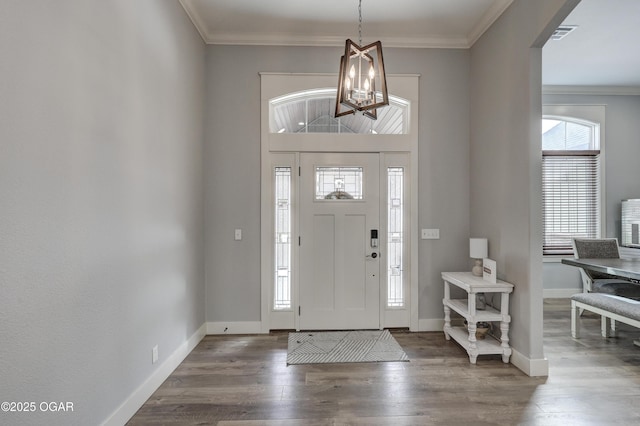 foyer entrance featuring visible vents, baseboards, ornamental molding, wood finished floors, and an inviting chandelier