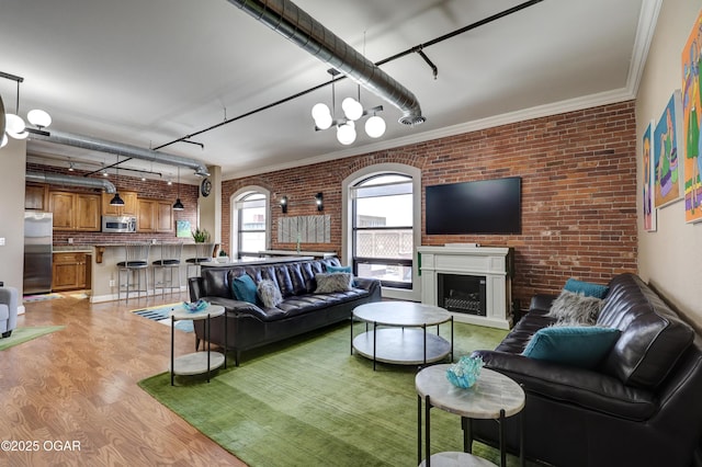 living room featuring crown molding, brick wall, rail lighting, and light wood finished floors