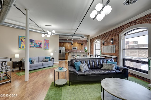 living area with visible vents, a notable chandelier, brick wall, rail lighting, and light wood finished floors