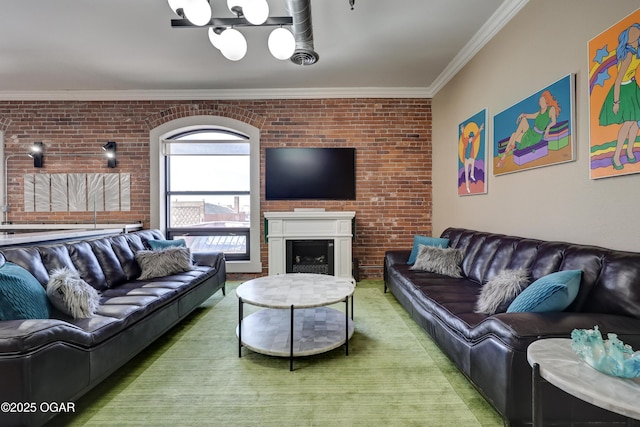 living room featuring a notable chandelier, a fireplace, brick wall, and ornamental molding