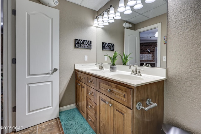 bathroom featuring tile patterned flooring, a drop ceiling, double vanity, a textured wall, and a sink