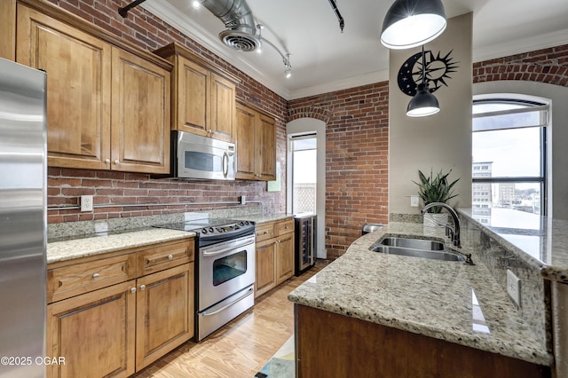 kitchen with brick wall, crown molding, beverage cooler, appliances with stainless steel finishes, and a sink