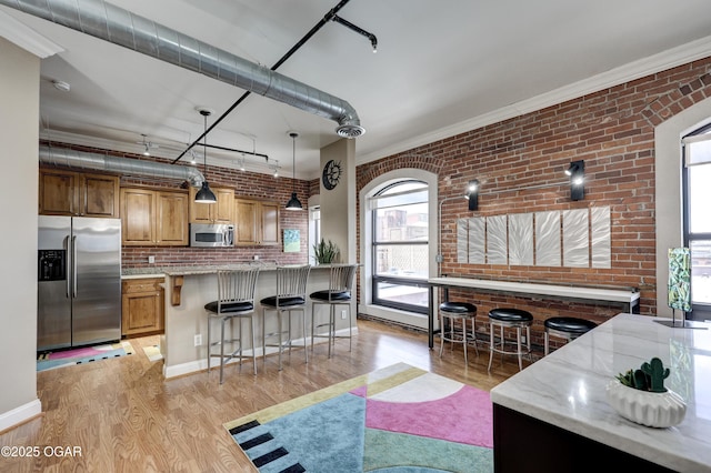 kitchen featuring light wood finished floors, brick wall, light stone countertops, a kitchen breakfast bar, and stainless steel appliances