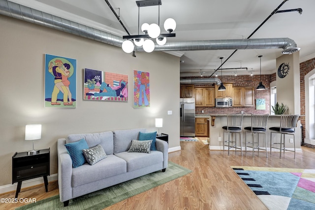 living room with baseboards, light wood-style floors, brick wall, and track lighting