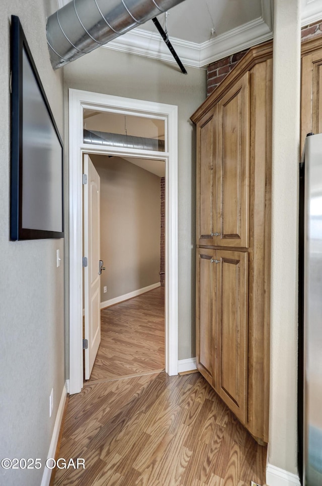 hallway featuring light wood-style flooring, crown molding, and baseboards