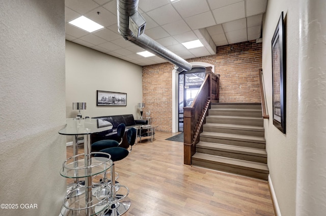 stairs with a drop ceiling, wood finished floors, and brick wall