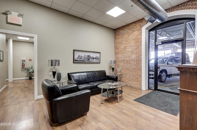 living area with a drop ceiling, baseboards, wood finished floors, and brick wall