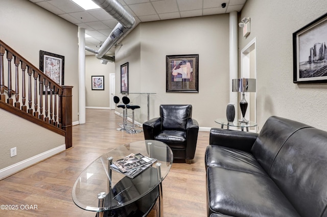 living room with wood finished floors, a paneled ceiling, baseboards, and a towering ceiling