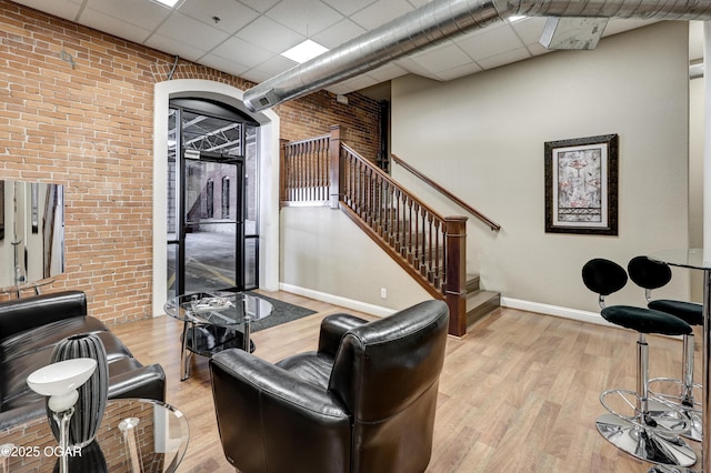 living area featuring light wood-type flooring, baseboards, brick wall, a paneled ceiling, and stairs