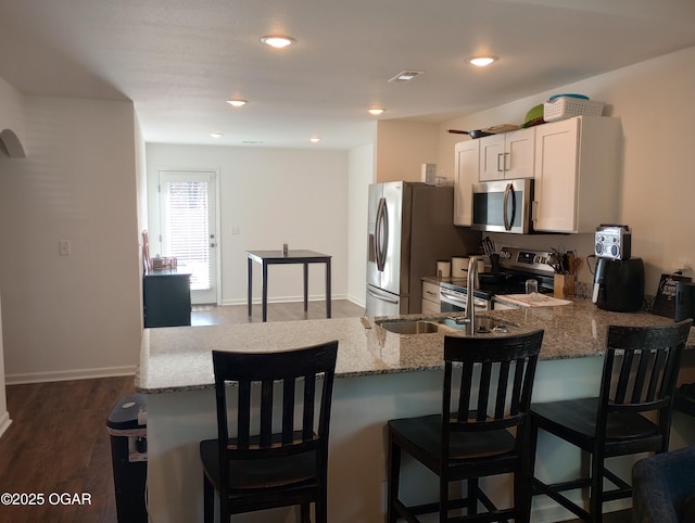 kitchen with light stone countertops, visible vents, a peninsula, appliances with stainless steel finishes, and a kitchen bar