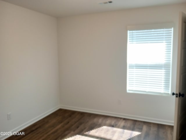 empty room featuring plenty of natural light, dark wood-style floors, and baseboards