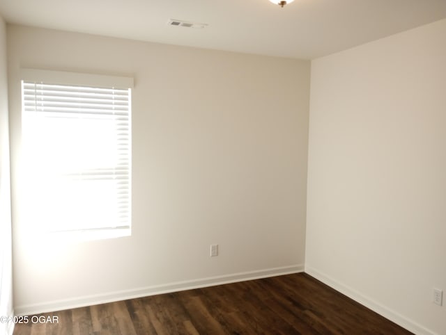 spare room featuring visible vents, baseboards, and dark wood-style flooring