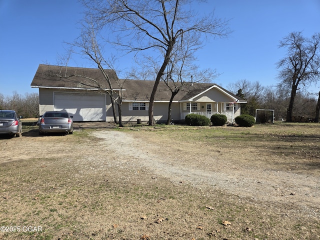 view of front facade with an attached garage, covered porch, dirt driveway, and a shingled roof