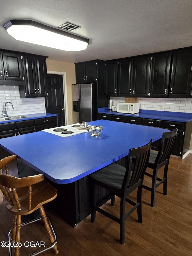 kitchen featuring dark cabinetry, white appliances, dark wood finished floors, a sink, and a kitchen bar