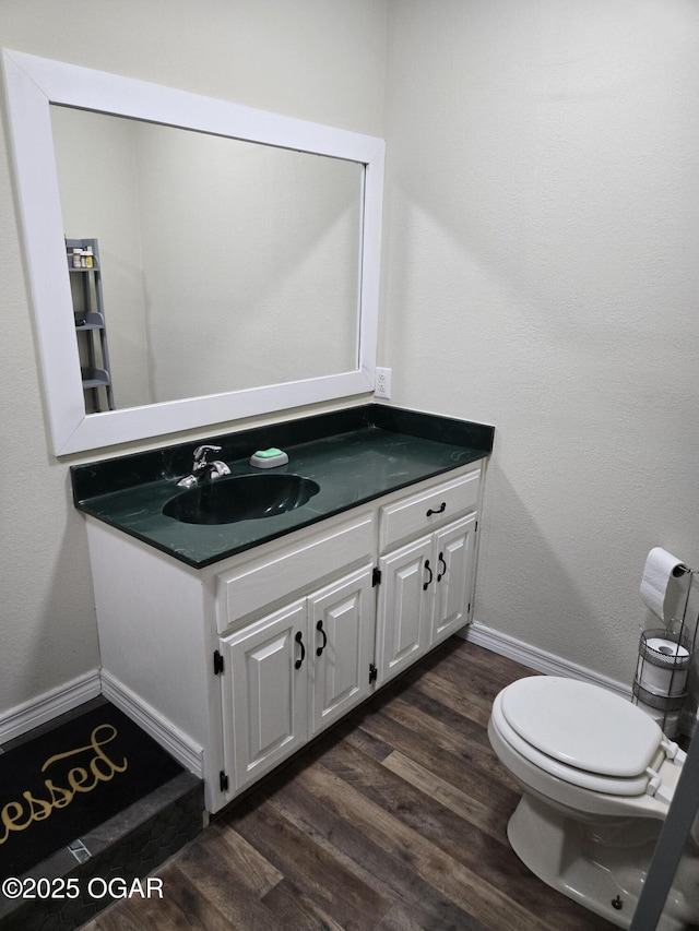 half bathroom with toilet, vanity, baseboards, and wood finished floors