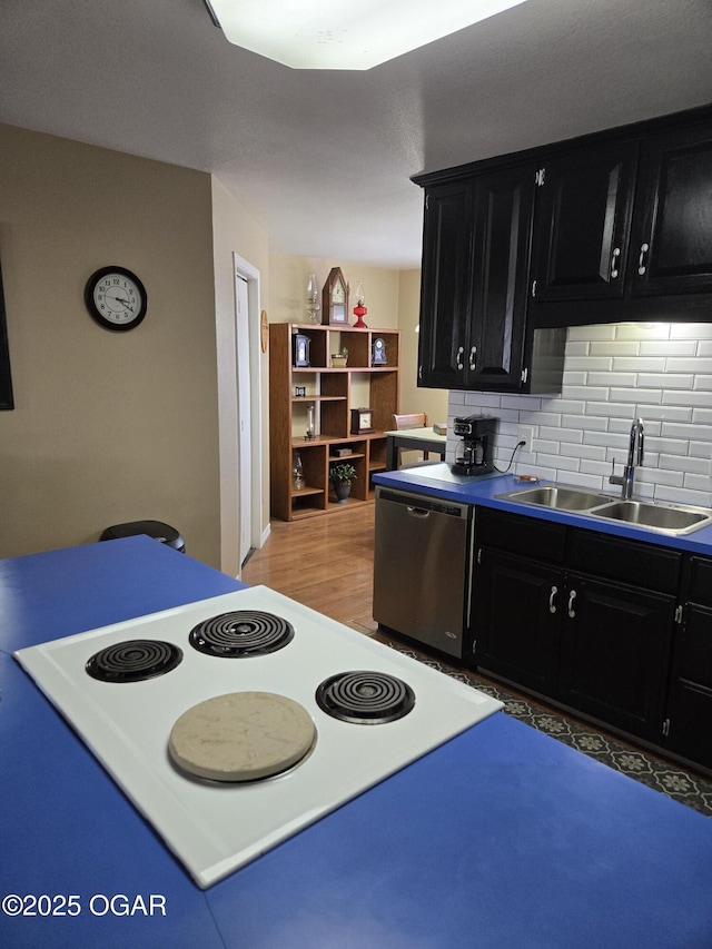 kitchen featuring dark cabinetry, light wood-style flooring, a sink, stainless steel dishwasher, and backsplash