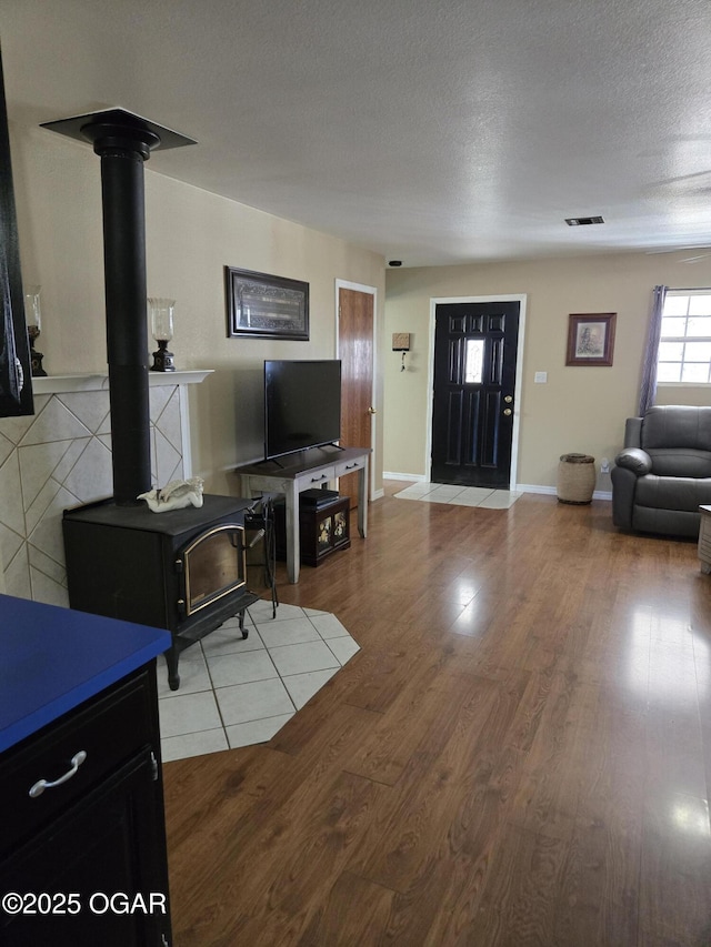 living room with light wood finished floors, visible vents, baseboards, a wood stove, and a textured ceiling