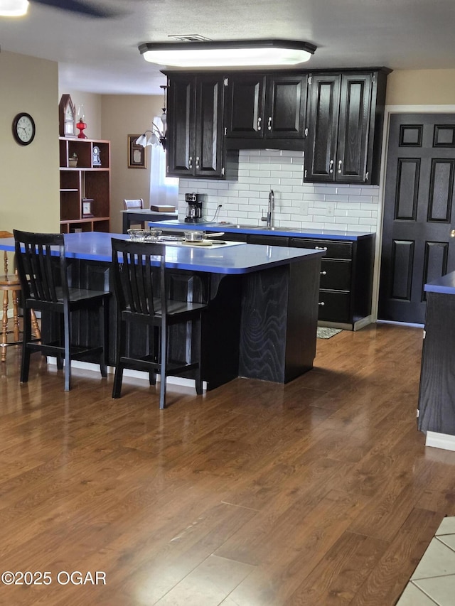 kitchen with tasteful backsplash, a center island, dark cabinetry, and wood finished floors