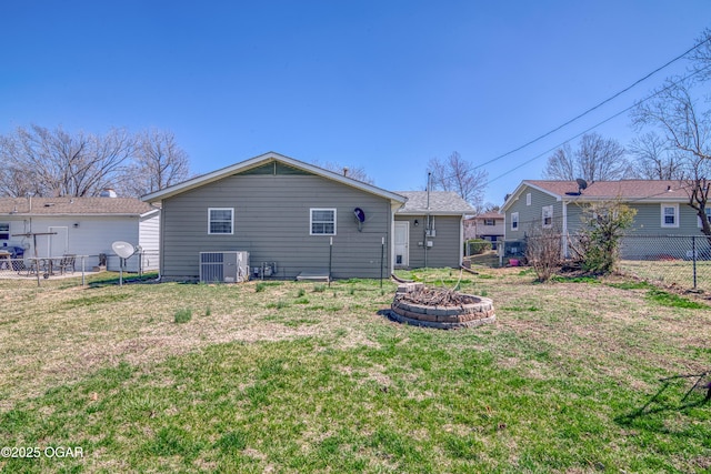 back of house featuring central air condition unit, a fire pit, fence, and a lawn