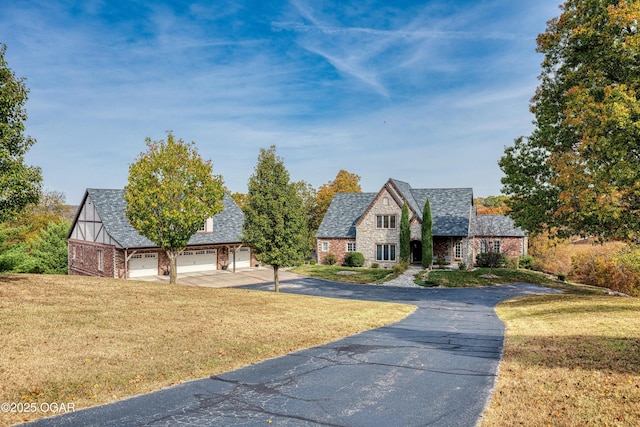 tudor-style house with aphalt driveway, a front yard, a garage, and stone siding