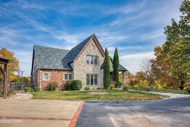 view of front of house featuring a front yard, a high end roof, fence, and stone siding