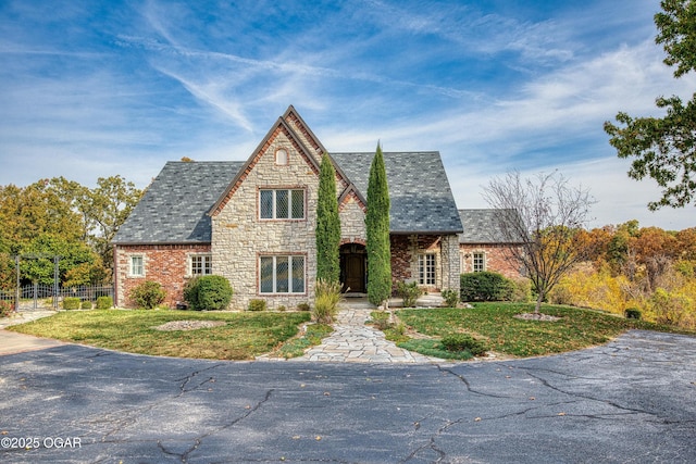 tudor-style house featuring a high end roof, stone siding, a front lawn, and fence